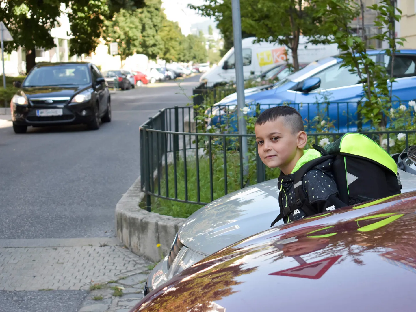 Schulweg Kind Parkende Autos 1440 Credit Jacquelinegodany Bub mit Schultasche schaut zwischen parkenden Autos auf die Straße