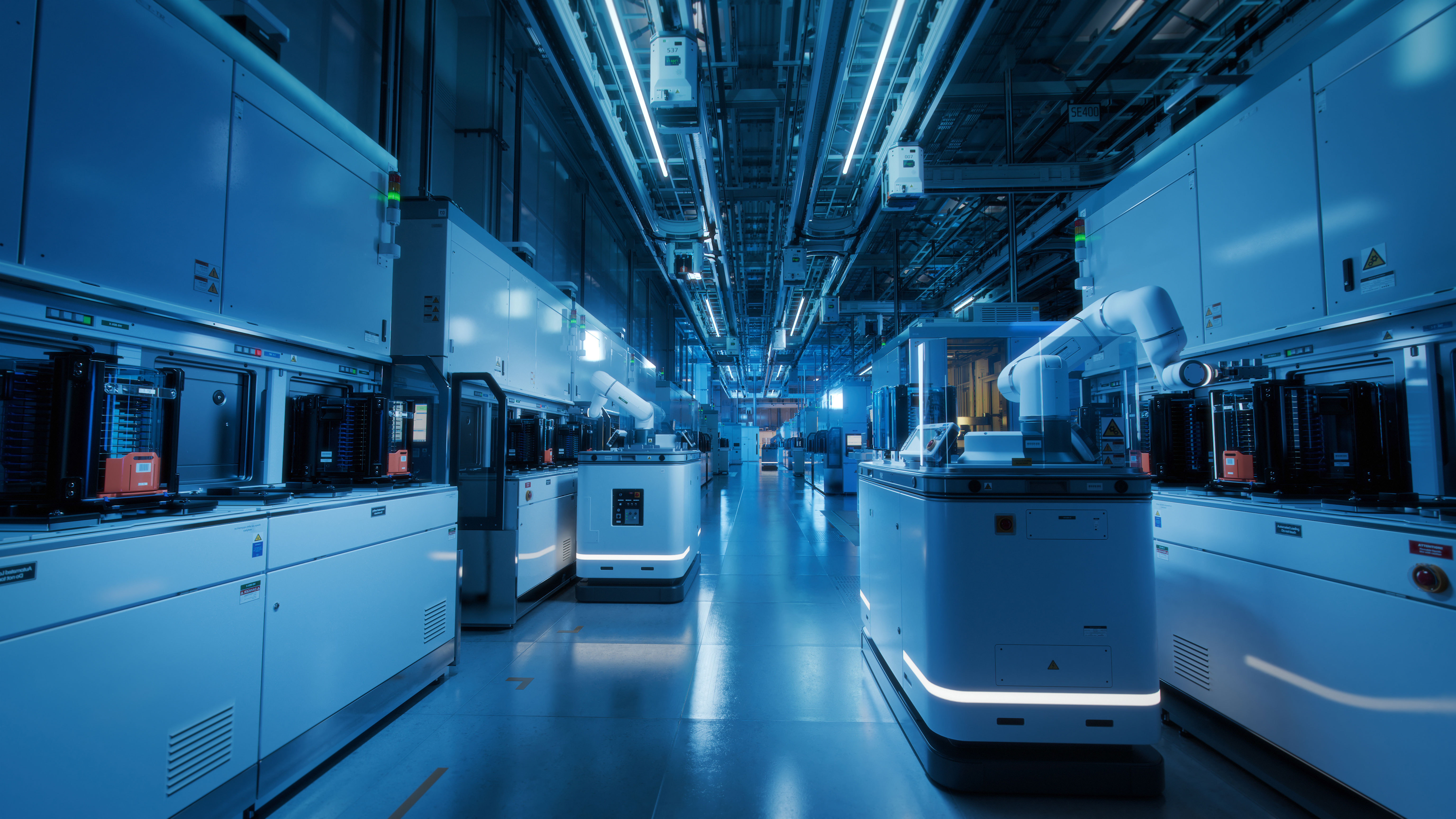 Weitwinkelaufnahme des Reinraums einer modernen Halbleiterfabrik. Automatisierte Roboter transportieren Wafer zwischen den Maschinen.