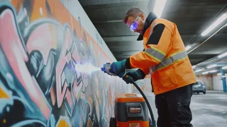 Laserreinigung1 Blau 1440 Credit KI Generiert Mit Midjourney Von M. Pravits Mann beim Laserreinigen einer Graffiti-Wand