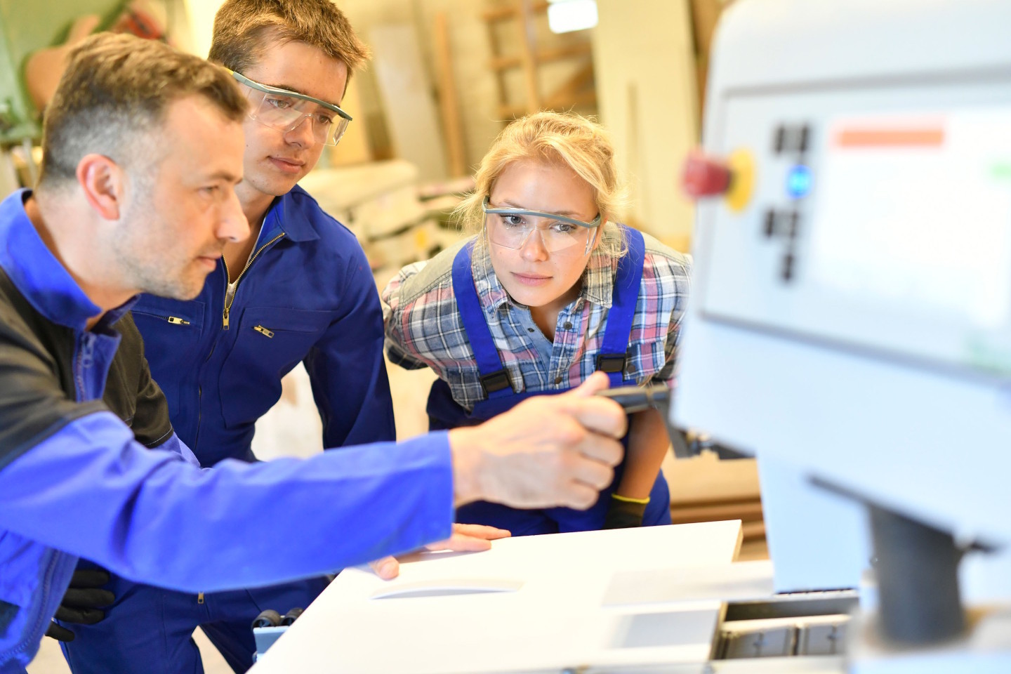 Ein Mann mittleren Alters zeigt einem männlichen und einer weiblichen Jugendlichen etwas an einer Maschine