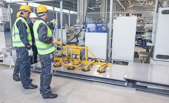 Arbeiter:innen heben eine Stahlplatte mithilfe eines Magnets.