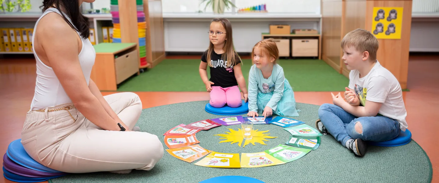 Pädagogin und drei Kindergartenkinder sitzen auf Sitzkissen im Sitzkreis