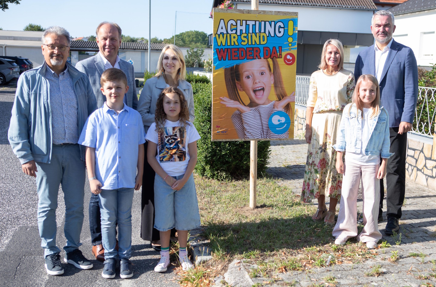 Eine Gruppe Erwachsener und Kinder. In der Mitte steht das Plakat mit dem Appell Achtung - Wir sind wieder da