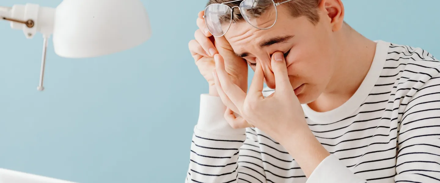 Ein Mann fasst sich bei der Büroarbeit mit den Finger an seine ermüdeten Augen Ein Mann fasst sich bei der Büroarbeit mit den Finger an seine ermüdeten Augen