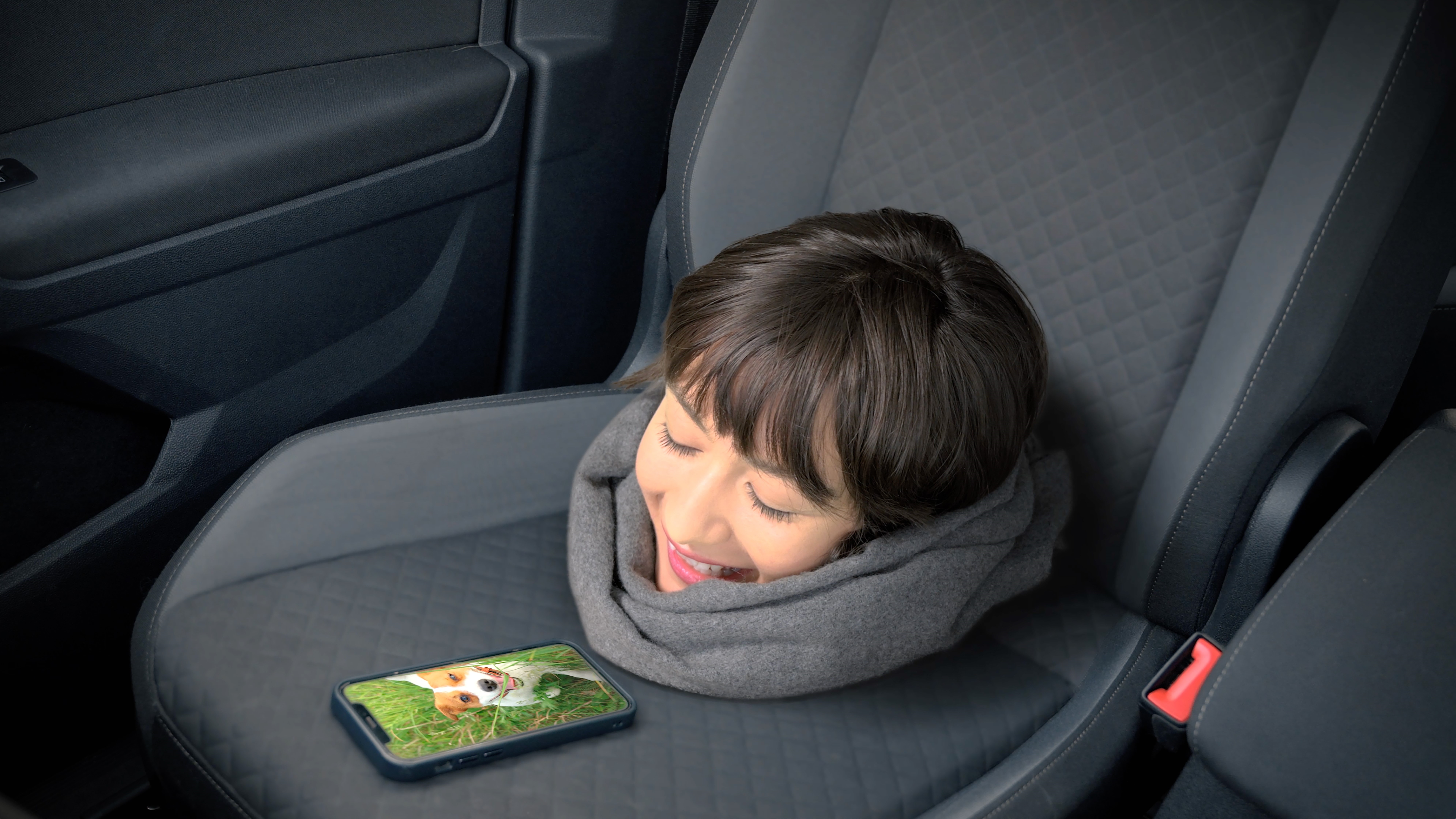 Fotomontage: Ein Frauenkopf mit Blick auf ein Smartphone liegt auf einem Autositz