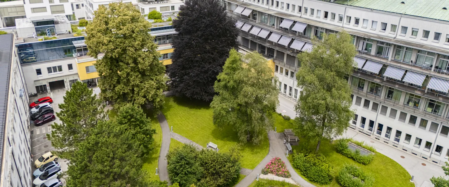 Aufnahme vom grünen Innenhof des UKH Salzburg inklusive eines Teils des Gebäudes Aufnahme vom grünen Innenhof des UKH Salzburg inklusive eines Teils des Gebäudes