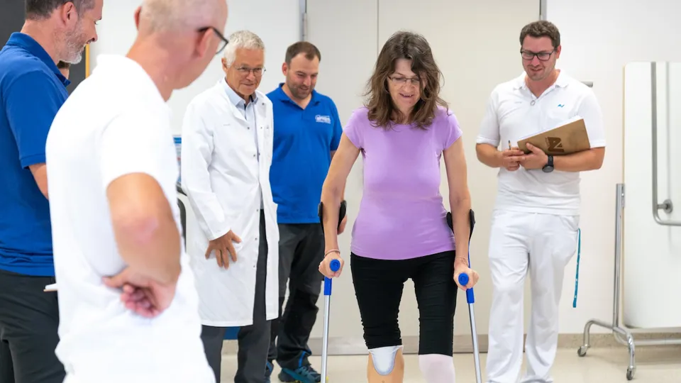 Patientin bei Gangübungen mit Gehhilfe unter Aufsicht mehrerer ärztlicher/therapeutischer Mitarbeiter des AUVA-RZ Häring Patientin bei Gangübungen mit Gehhilfe unter Aufsicht mehrerer ärztlicher/therapeutischer Mitarbeiter des AUVA-RZ Häring