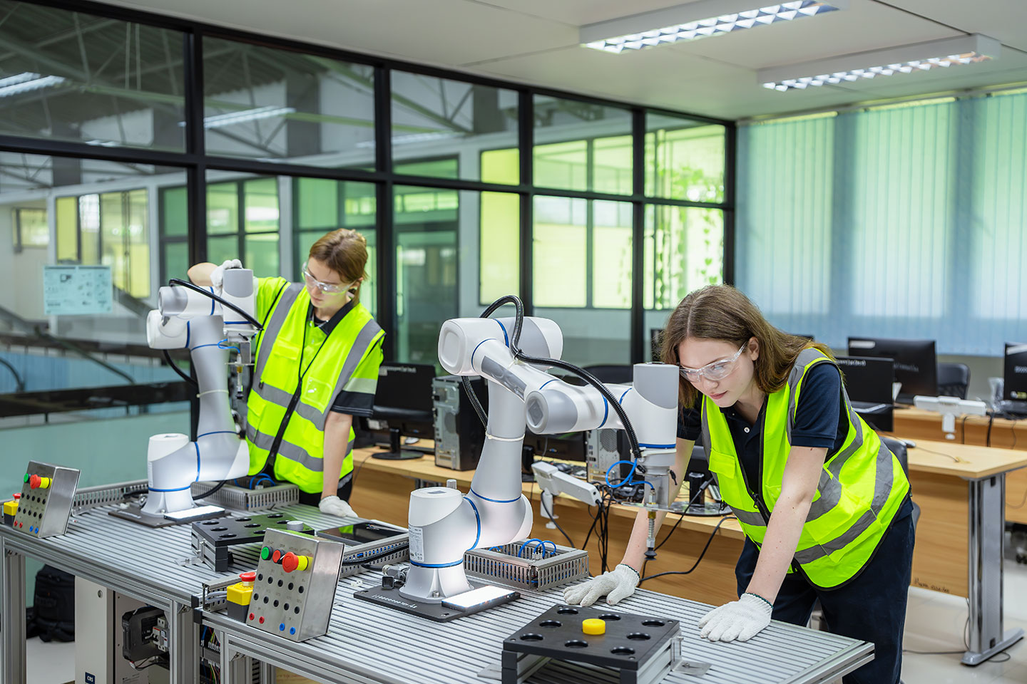 Zwei Frauen in Warnwesten hantieren mit Robotern, die auf einem Tisch stehen.
