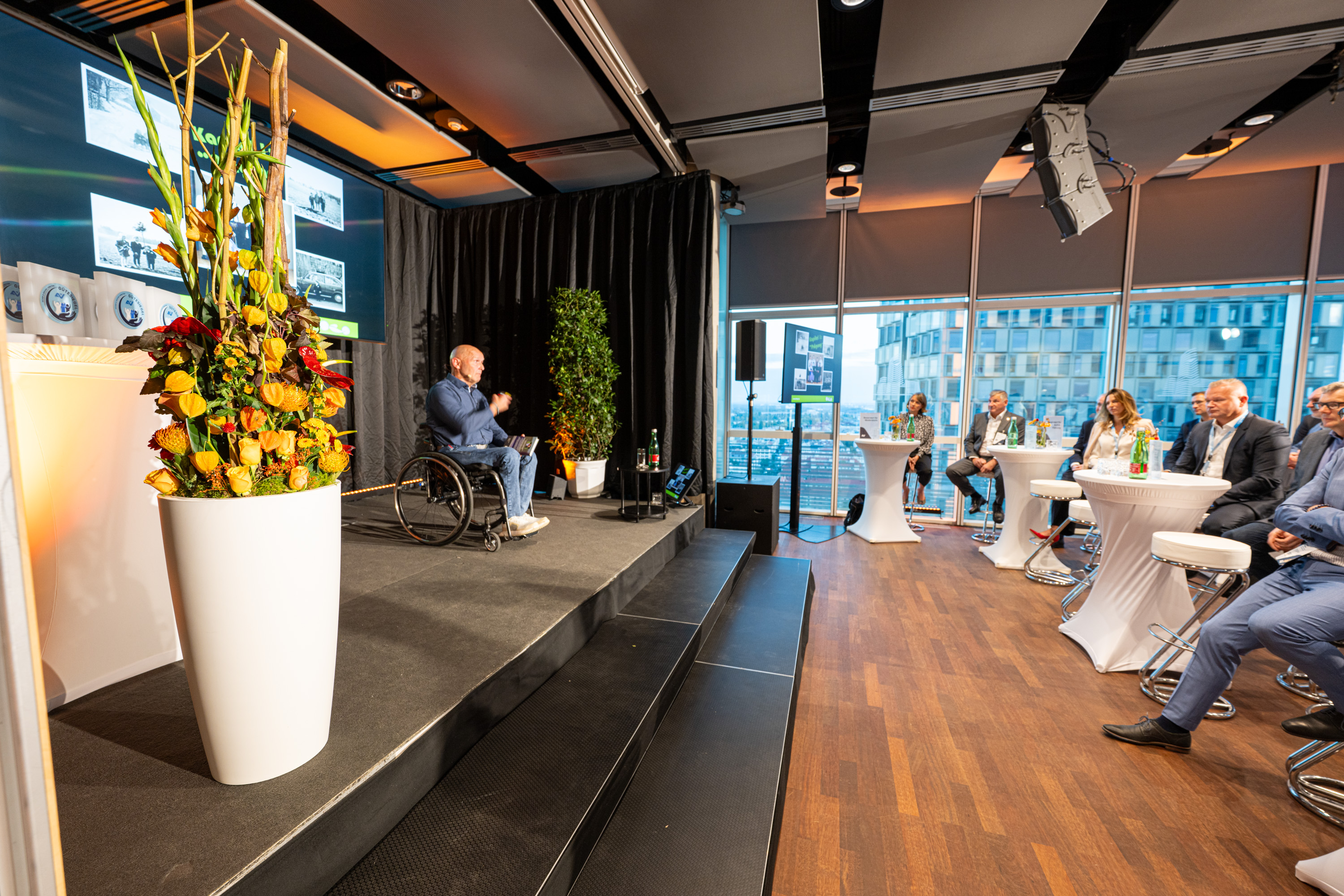 Ein Mann in einem Rollstuhl sitzt auf einer Bühne und spricht zum Publikum