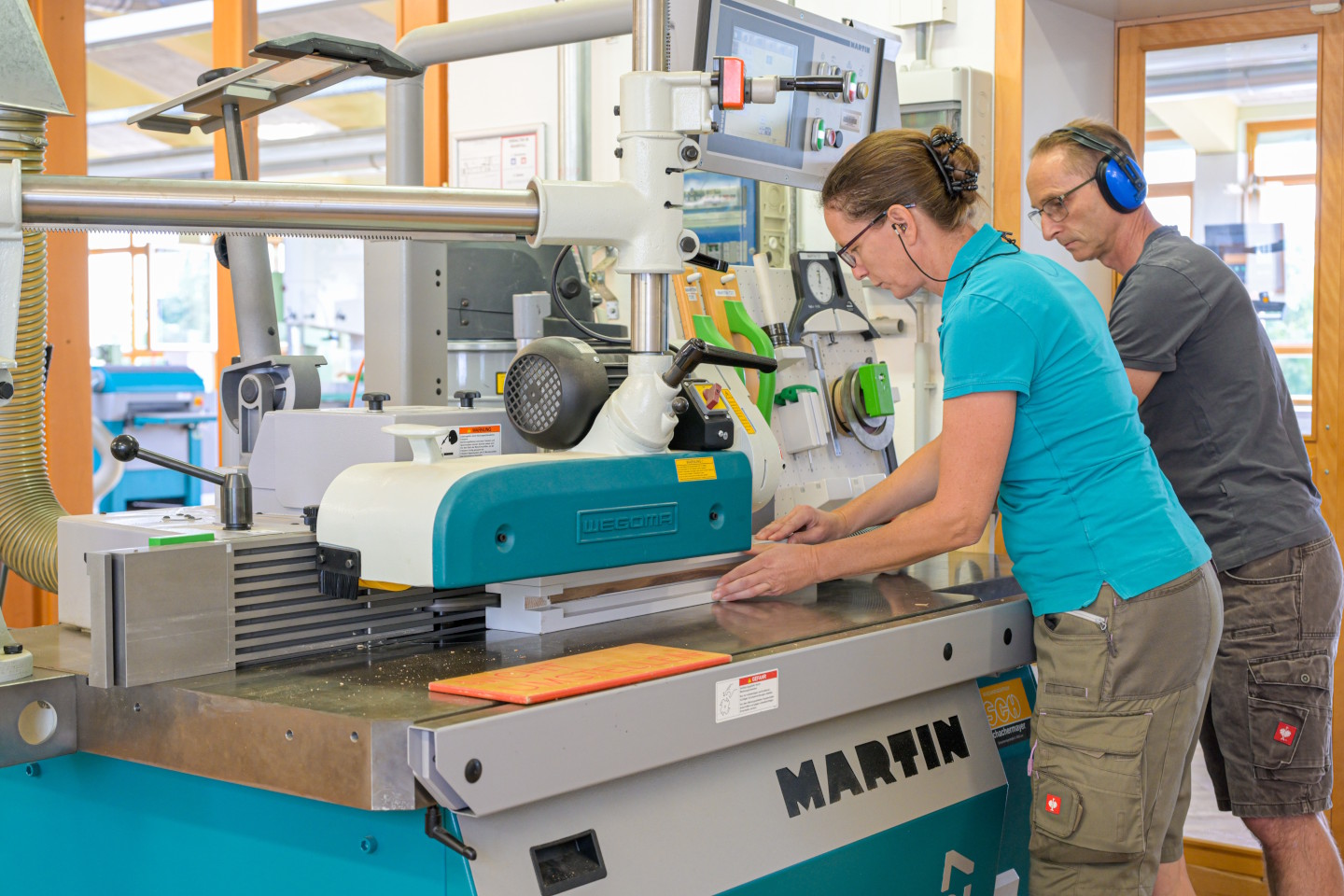 drei Erwachsene beim Arbeiten an einer Holzkreissäge