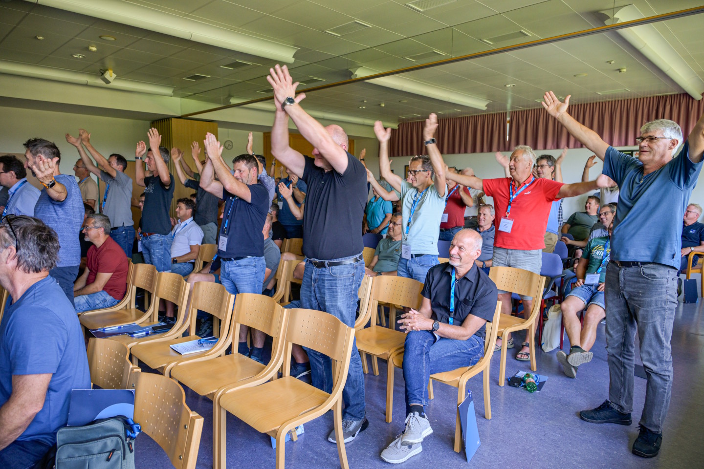 Mehrere Menschen in einem Vortragssaal stehen und halten die Arme in die Luft