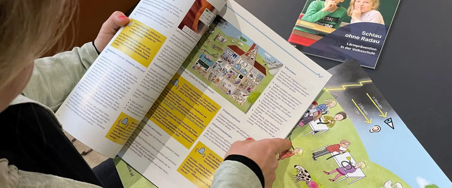 Eine Person sitzt an einem Tisch und blättert durch eine AUVA-Broschüre für Kinder.