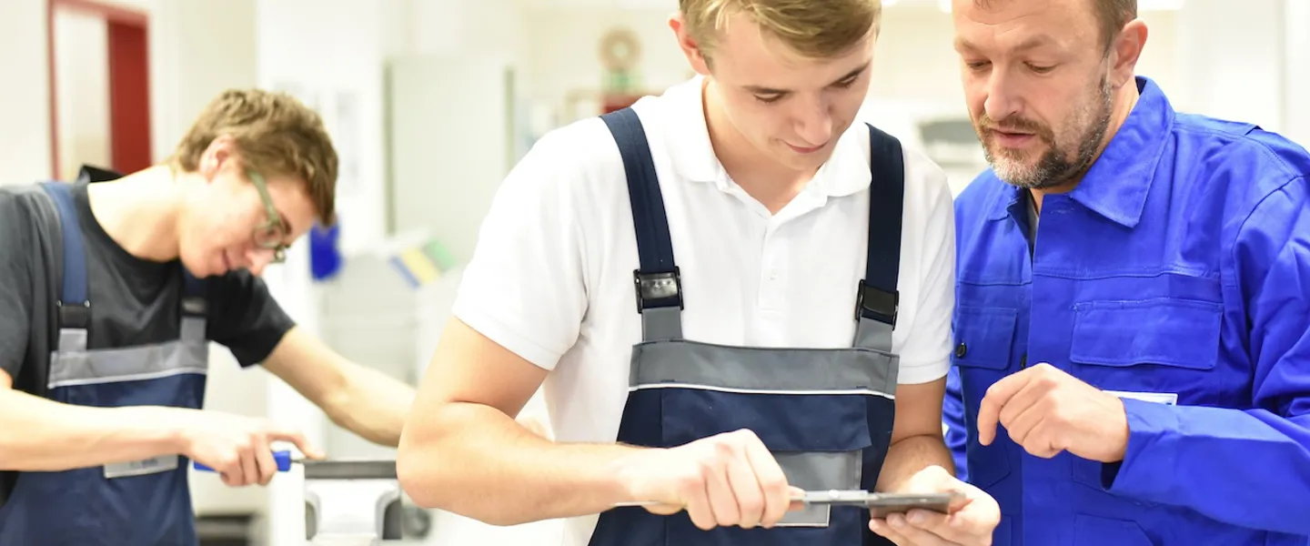 Männer in Arbeitskleidung überprüfen in einer Werkstatt ein Werkstück Männer in Arbeitskleidung überprüfen in einer Werkstatt ein Werkstück
