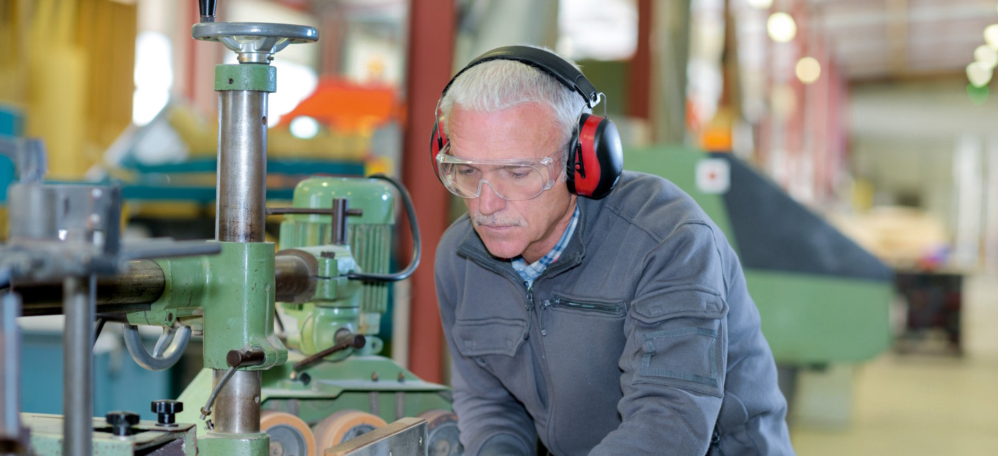 Ein älterer Mann mit Kapselgehörschutz arbeitet an einer Maschine