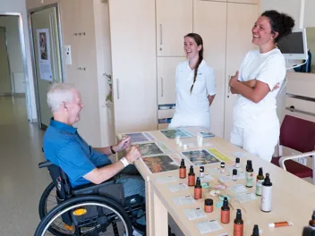 RH Pflege (1) - Rollstuhlpatient Aromatherapiegespräch VDR 053090923 (1) Lachender Patient im Rollstuhl mit Pflegekräften während Aromatherapiegespräch im AUVA-RZ Häring