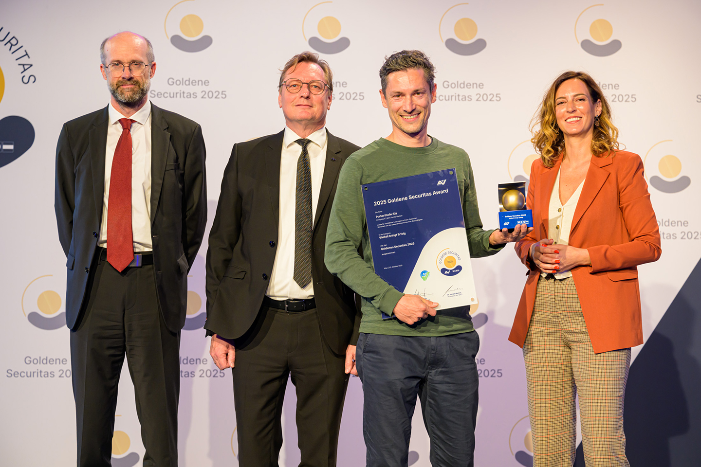 Eine Gruppe von Erwachsenen steht vor der Goldene Securitas-Logowand