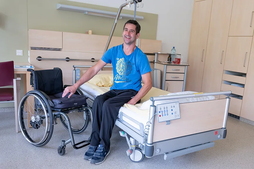Patient sitzend auf Patientenbett mit nebenstehendem Rollstuhl Patient sitzend auf Patientenbett mit nebenstehendem Rollstuhl