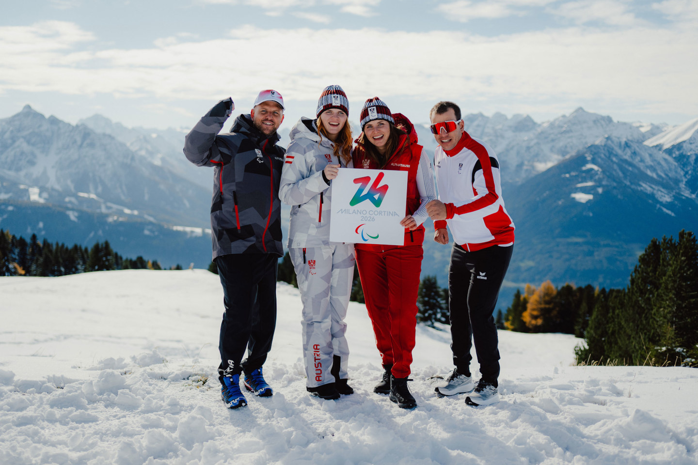 Team aus 4 Para-Skiathleten des ÖPC steht an einer Skipiste und zeigt ein Schild mit Aufschrift Milano Cortina 2026 in die Kamera