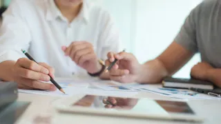 Zwei nur halb sichtbare Personen arbeiten an mehreren auf einem Schreibtisch liegenden Dokumenten Zwei nur halb sichtbare Personen arbeiten an mehreren auf einem Schreibtisch liegenden Dokumenten