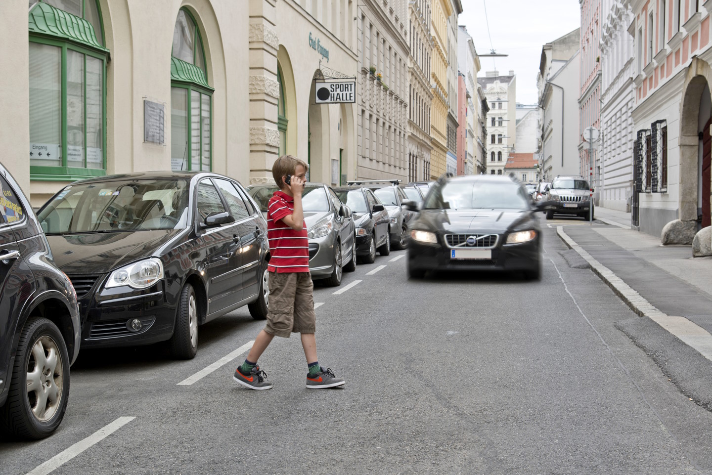 Kind mit Handy quert eine Fahrbahn vor einem herannahenden Auto