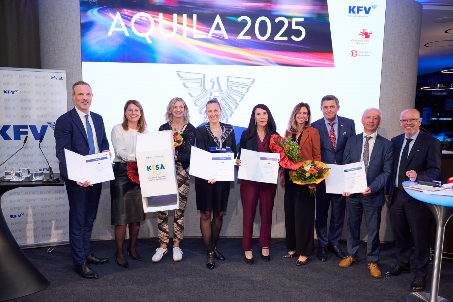 Eine Gruppe von Menschen auf einer Bühne. Sie halten Urkunden und Blumensträuße in der Hand