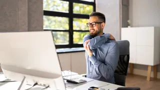 Mann arbeitet im Mobile Office und dehnt seine Schulter.