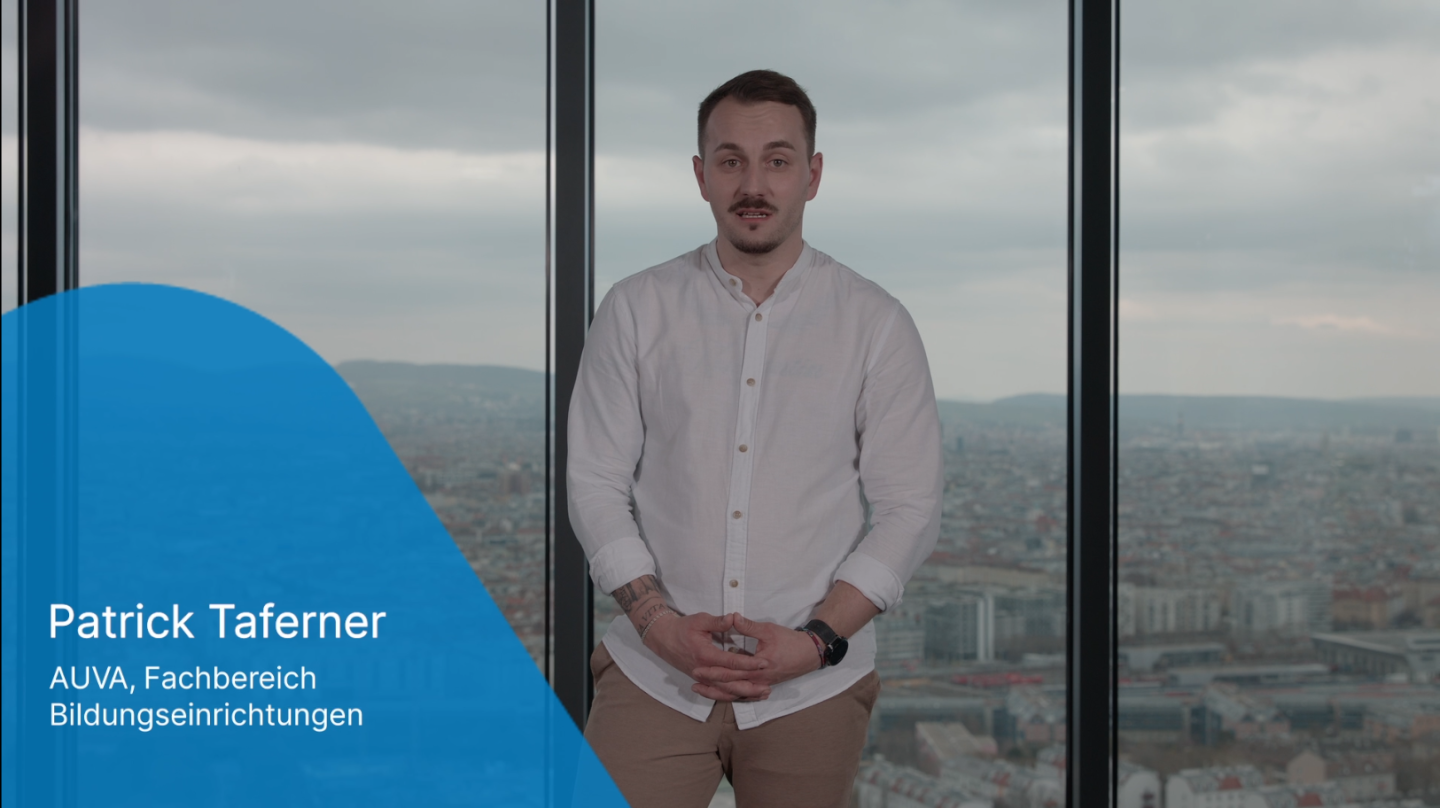 Ein junger Mann steht vor einer großen Fensterfront und schaut in Richtung Kamera