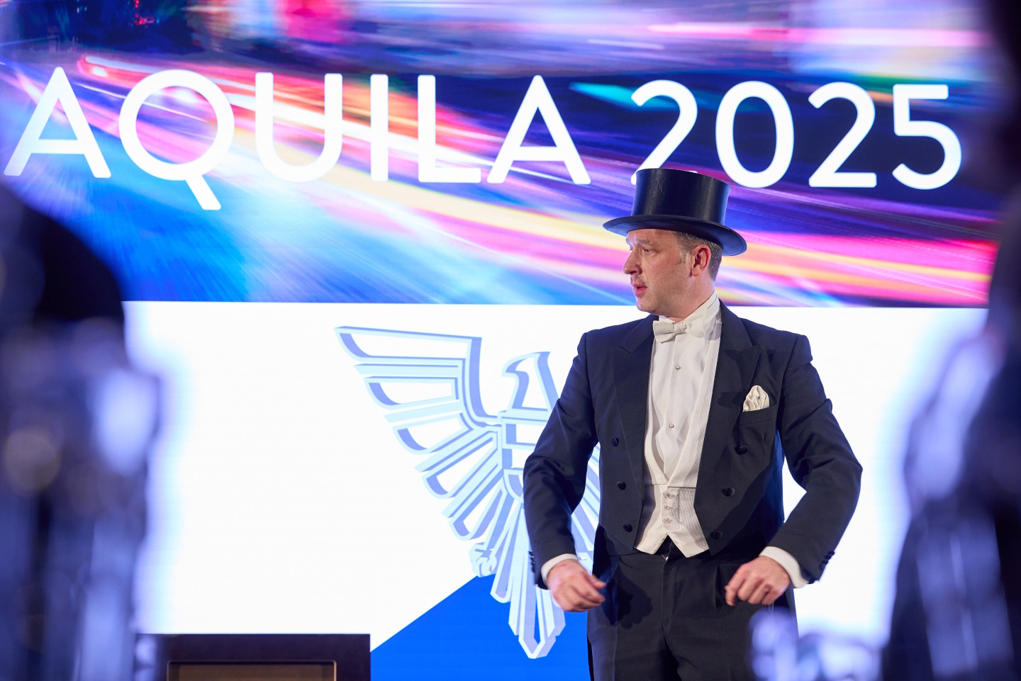 Ein Mann in Frack und Zylinder auf der Bühne vor einer Leinwand