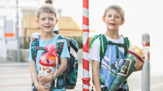 Mein-sicherer-Schulweg.at Zwei Schulanfänger warten mit ihren Schultüten an einer Kreuzung auf ihrem Schulweg.