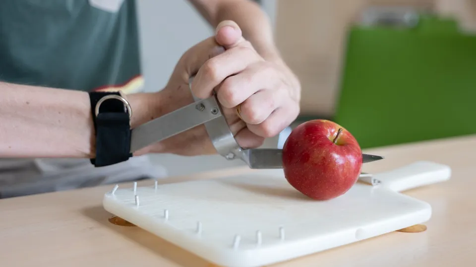 Ein Patient bei einer ergotherapeutischen Übung mit Schneidwerkzeug, Schneidbrett und einem Apfel Ein Patient bei einer ergotherapeutischen Übung mit Schneidwerkzeug, Schneidbrett und einem Apfel