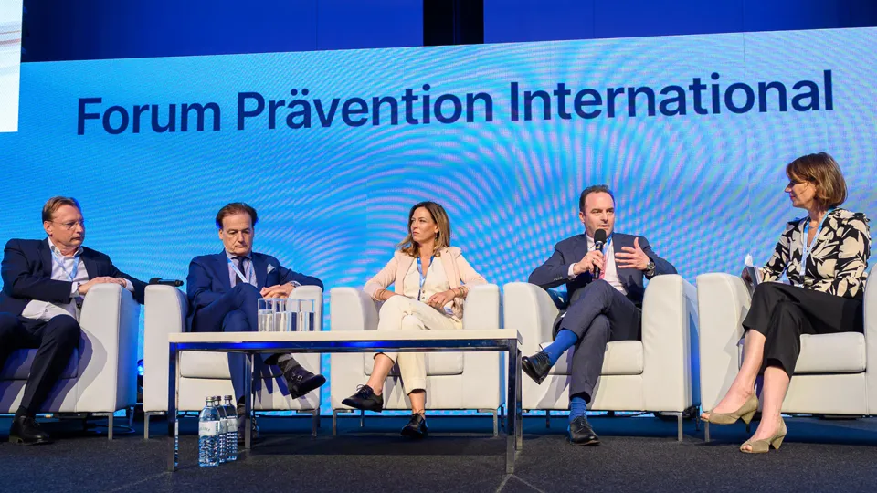 Fünf Personen sitzen auf Stühlen am Podium. Im Hintergrund steht "Forum Prävention International"