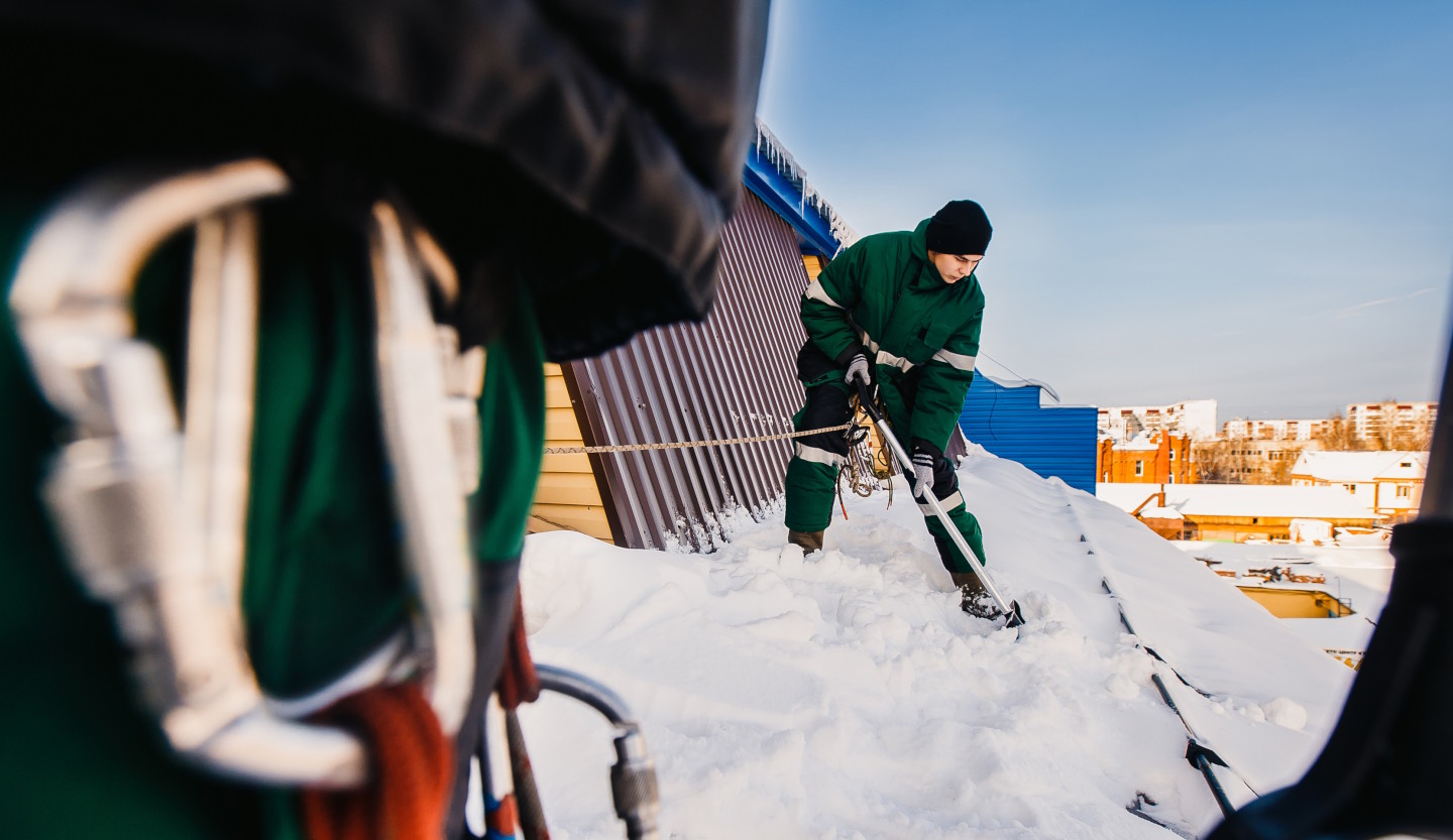 Ein Mann schaufelt Schnee von einem Dach