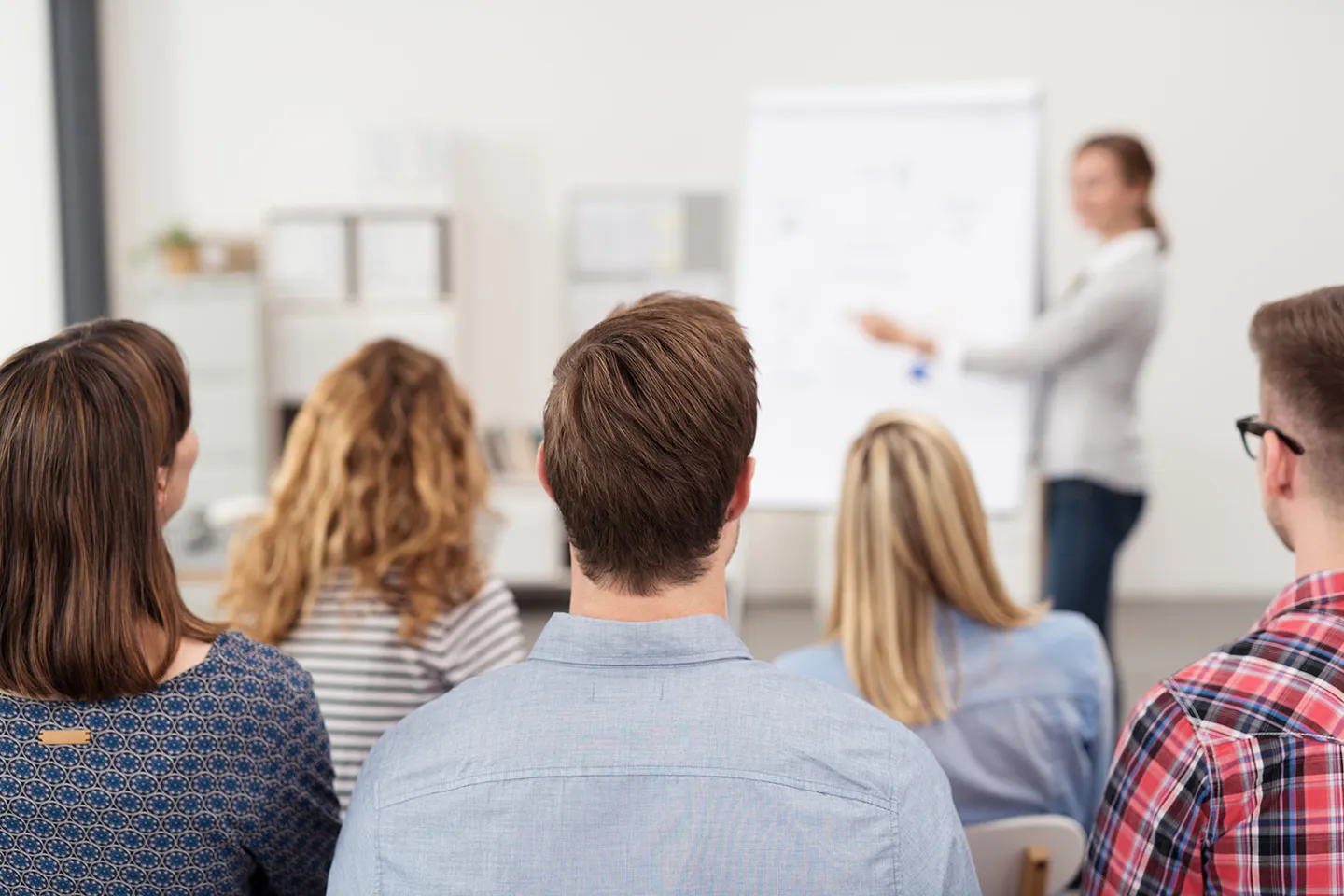 4.3_Schulungen_Veranstaltungen_AdobeStock_86512117.jpeg Seminarteilnehmer hören aufmerksam der Fachexpertin zu, die am Flipchart erklärt.