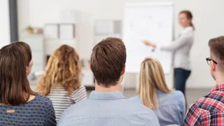 4.3_Schulungen_Veranstaltungen_AdobeStock_86512117.jpeg Seminarteilnehmer hören aufmerksam der Fachexpertin zu, die am Flipchart erklärt.