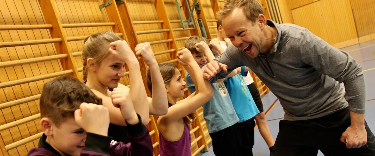 Ein Trainer bei einer spielerischen Übung mit mehreren Kindern in einer Turnhalle Ein Trainer bei einer spielerischen Übung mit mehreren Kindern in einer Turnhalle