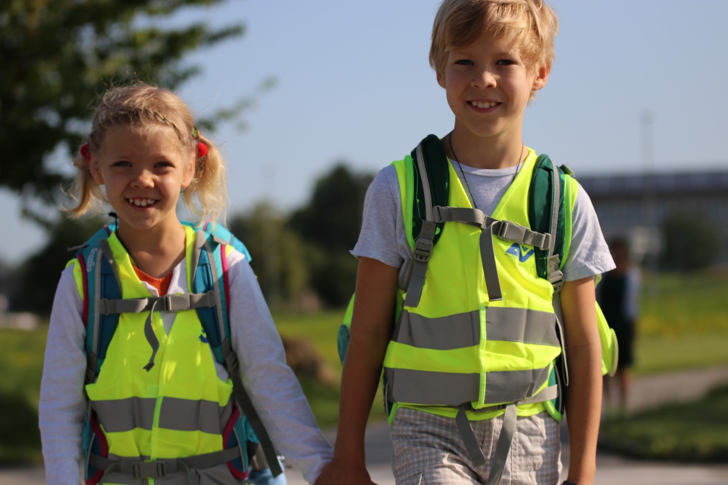 Ein Bub und ein Mädchen gehen mit Schultaschen und Warnwesten bekleidet Hand in Hand