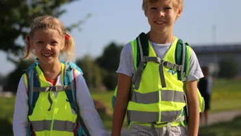 Warnwesten AUVA 1440 Cordas Pernjak Ein Bub und ein Mädchen gehen mit Schultaschen und Warnwesten bekleidet Hand in Hand