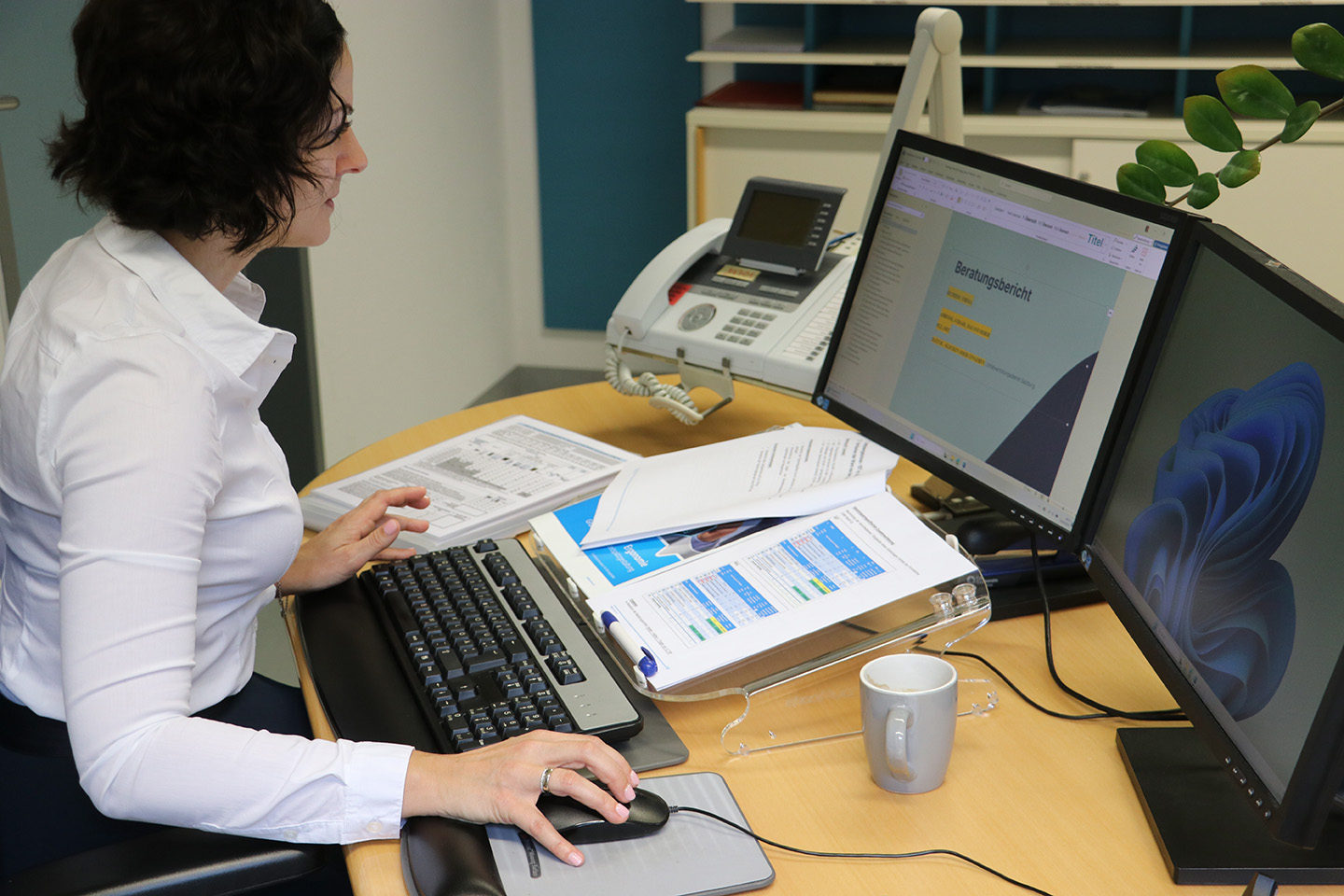Eine Frau sitzt an einem Schreibtisch und schaut auf einen Bildschirm.