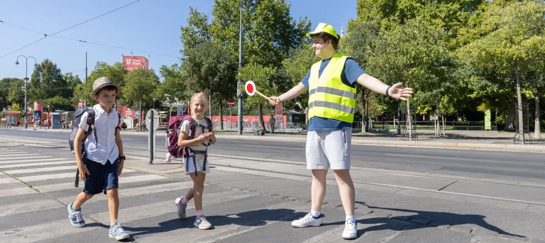 056 20250820 1440 KFV APA Fotoservice Juhasz Schülerlotse mit Warnweste und Kelle und zwei Schulkinder am Zebrastreifen