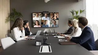 Gruppe von Mitarbeiter:innen führen im Konferenzraum eine Online Besprechung mit mehreren Kolleg:innen.